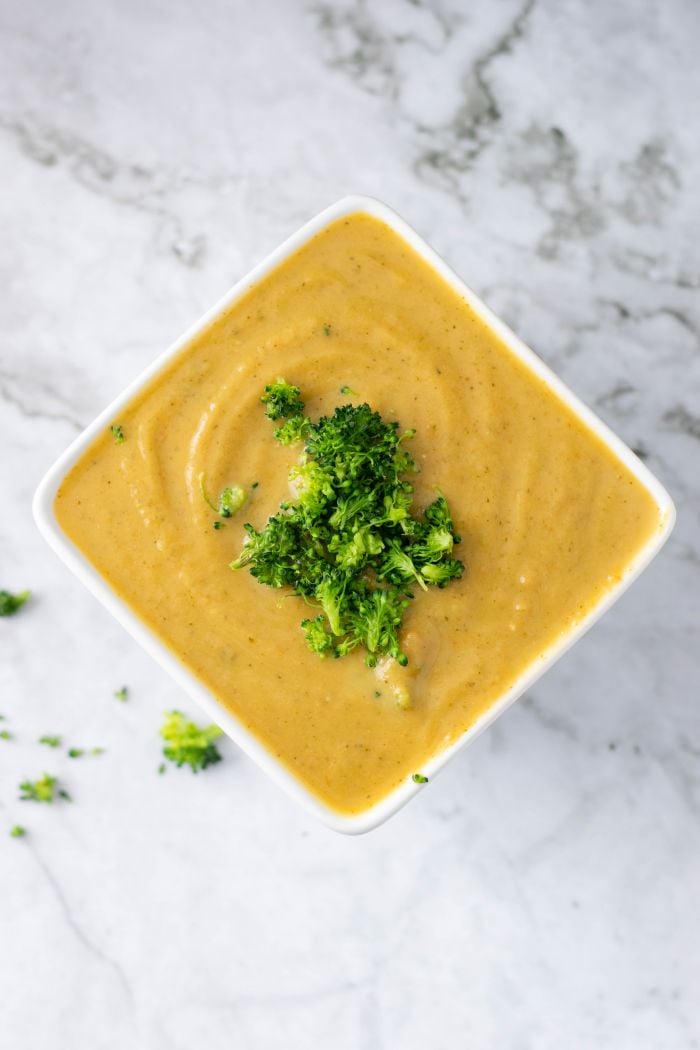 A top down view of broccoli cheddar soup in a square bowl, topped with bits of broccoli